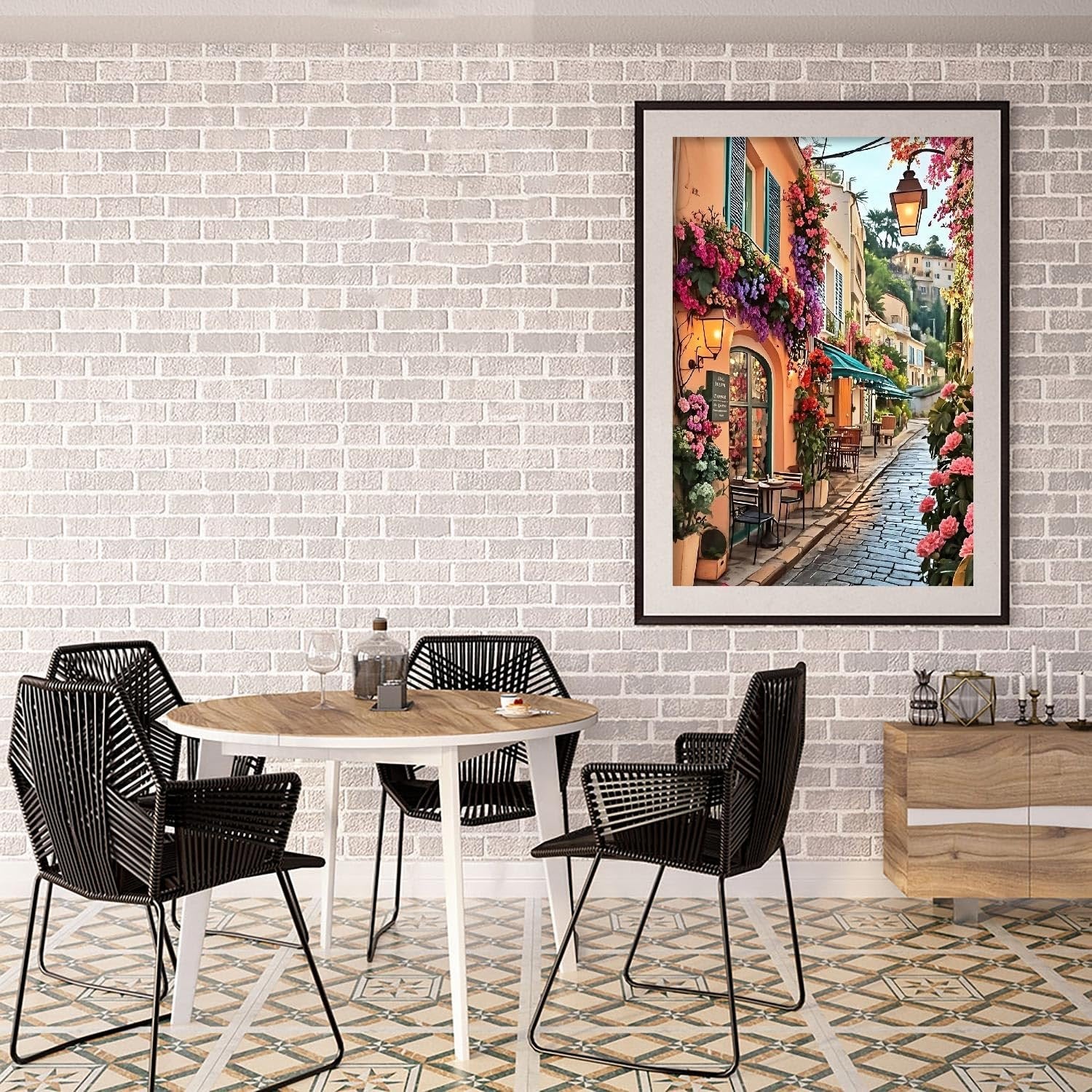 Framed diamond painting of a flower-lined street in a European town, displayed above a dining table with chairs.
