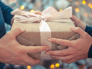 Two people holding a wrapped gift box with a light pink ribbon and bow, bokeh lights in background