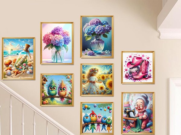 Collection of framed diamond art paintings displayed on a wall, featuring beach scene, flowers, birds, girl in sunflowers, cowboy boots, and a grandma sewing.
