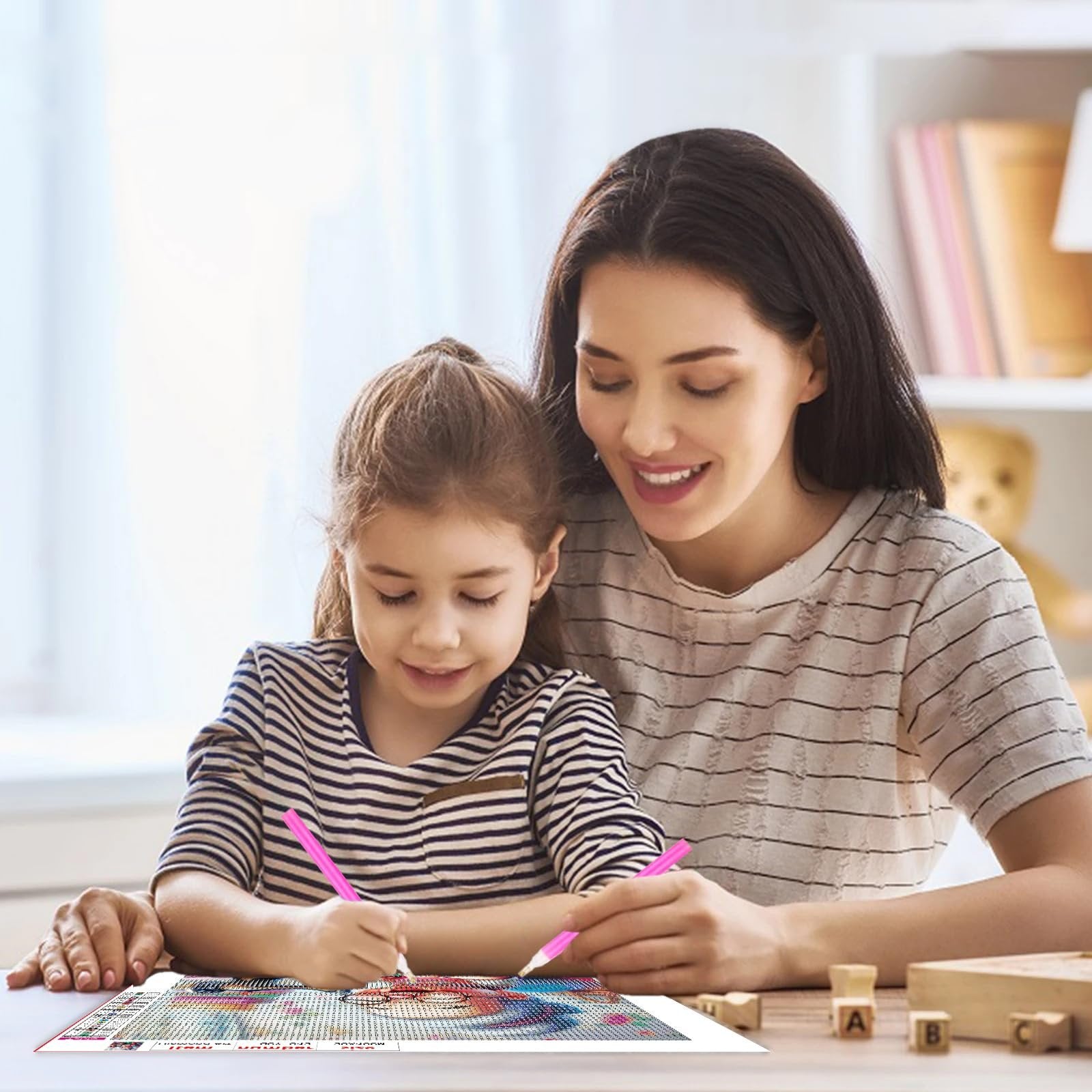Mother and daughter doing a diamond art kit together at a table, smiling and focused on the canvas.