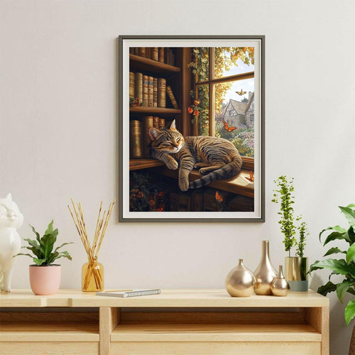 Cat sleeping on a windowsill next to bookshelves with a view of a cottage and garden outside.