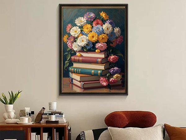 Framed painting of a bouquet of colorful flowers atop a stack of vintage books, displayed on a wall above a wooden cabinet.