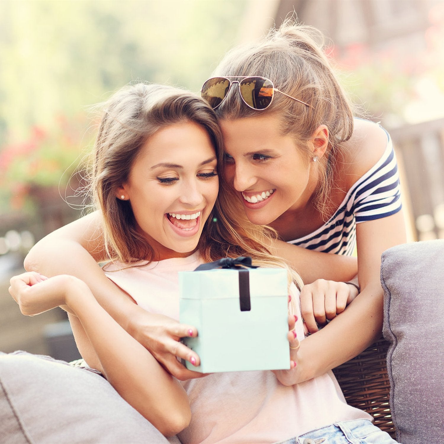 Two smiling women sharing a light blue gift box outdoors