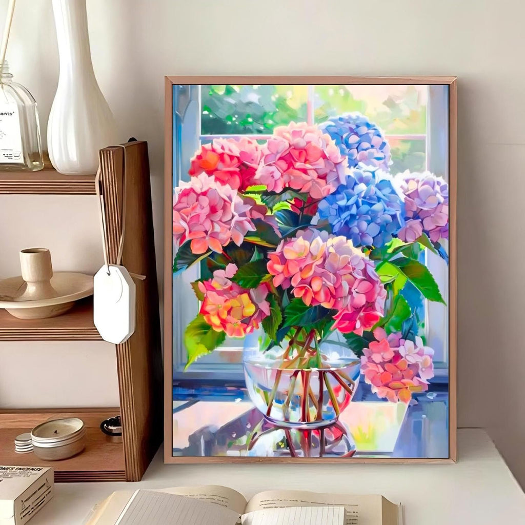 Diamond painting kit of a vase filled with pink and blue hydrangeas on a table by a window.