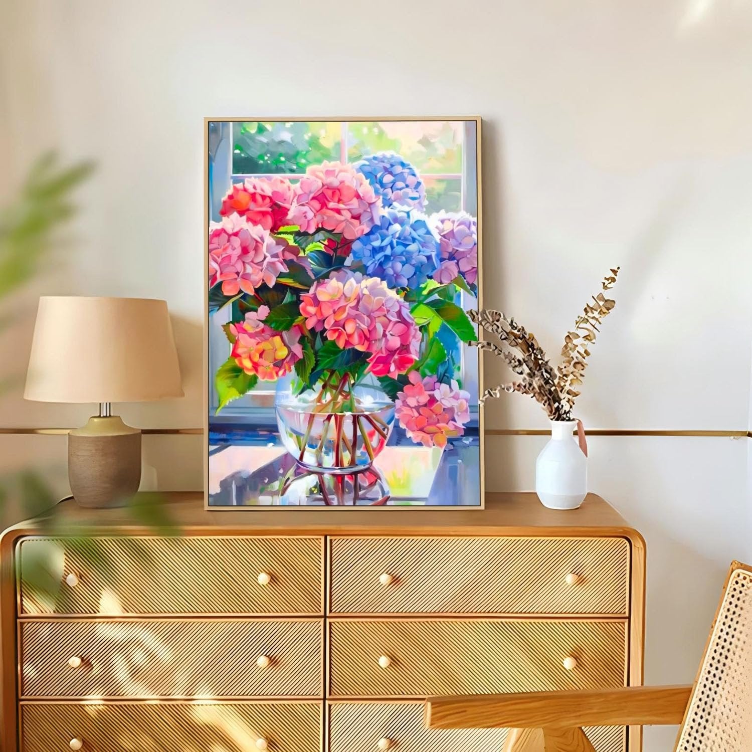 Framed diamond painting of pink and blue hydrangeas in a glass vase on a dresser, next to a lamp and dried flowers.
