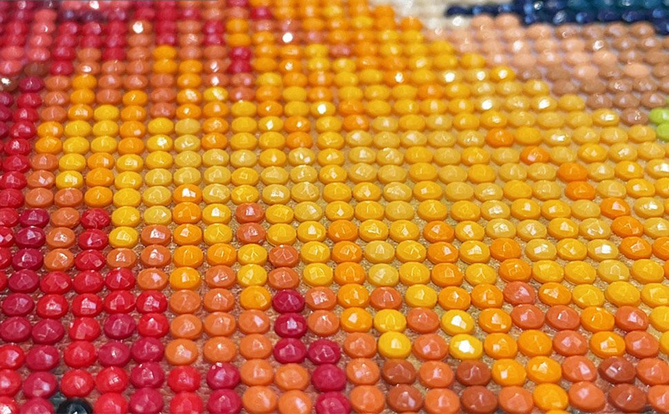 Close-up of a diamond painting canvas showing rows of round, faceted beads in shades of red, orange, and yellow, creating a sunset beach scene.