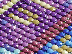 Close-up of a diamond painting kit with colorful purple, blue, red, and yellow gems arranged in a pattern.