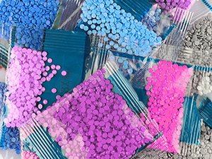 Close-up of small plastic bags filled with colorful diamond painting drills in blue, purple, pink, and gray.