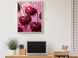Framed 12x16in full drill diamond painting kit featuring a close-up of glossy red cherries on a pink background, displayed on a wall above a desk.