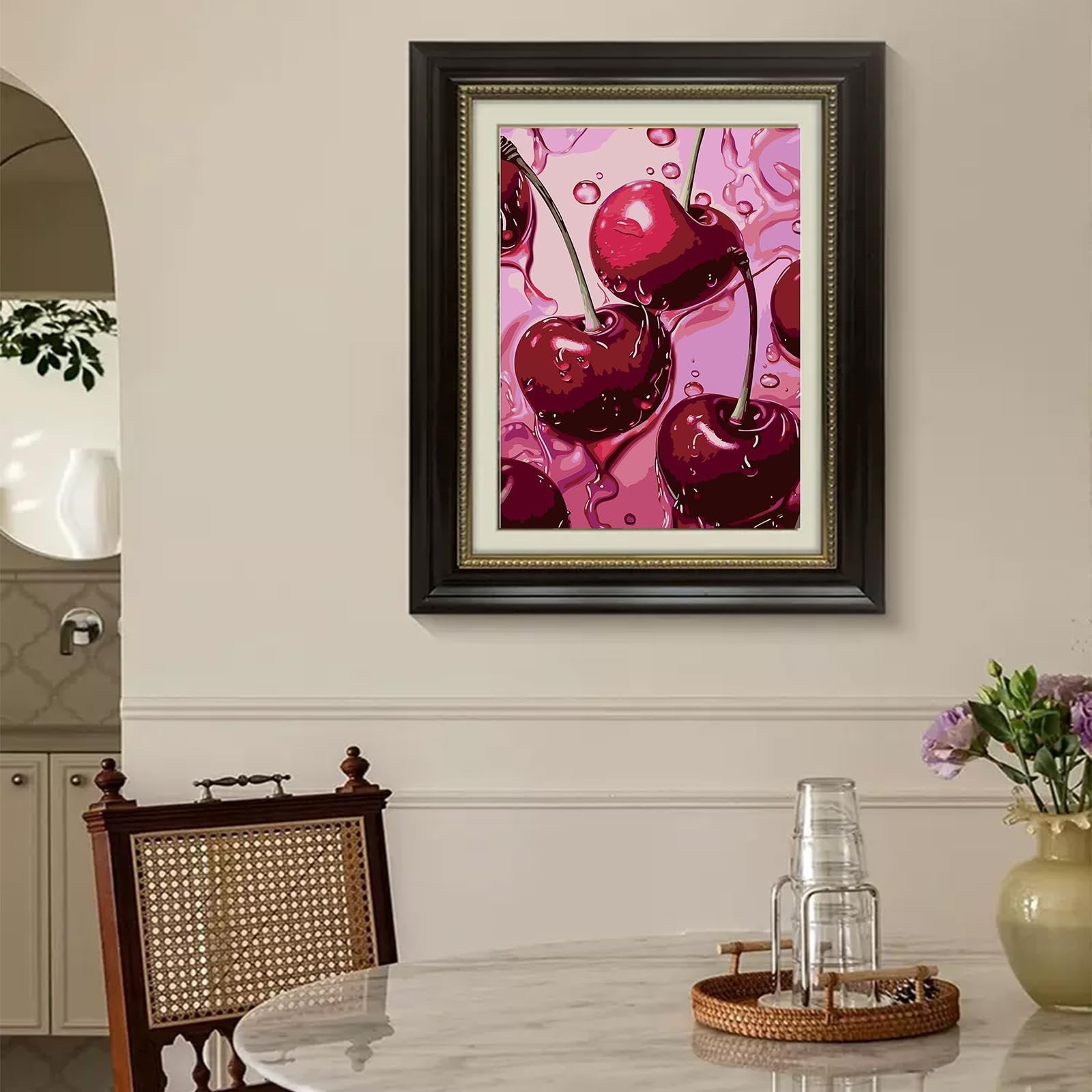 Framed diamond painting of cherries with water droplets on a pink background, displayed in a dining room setting.