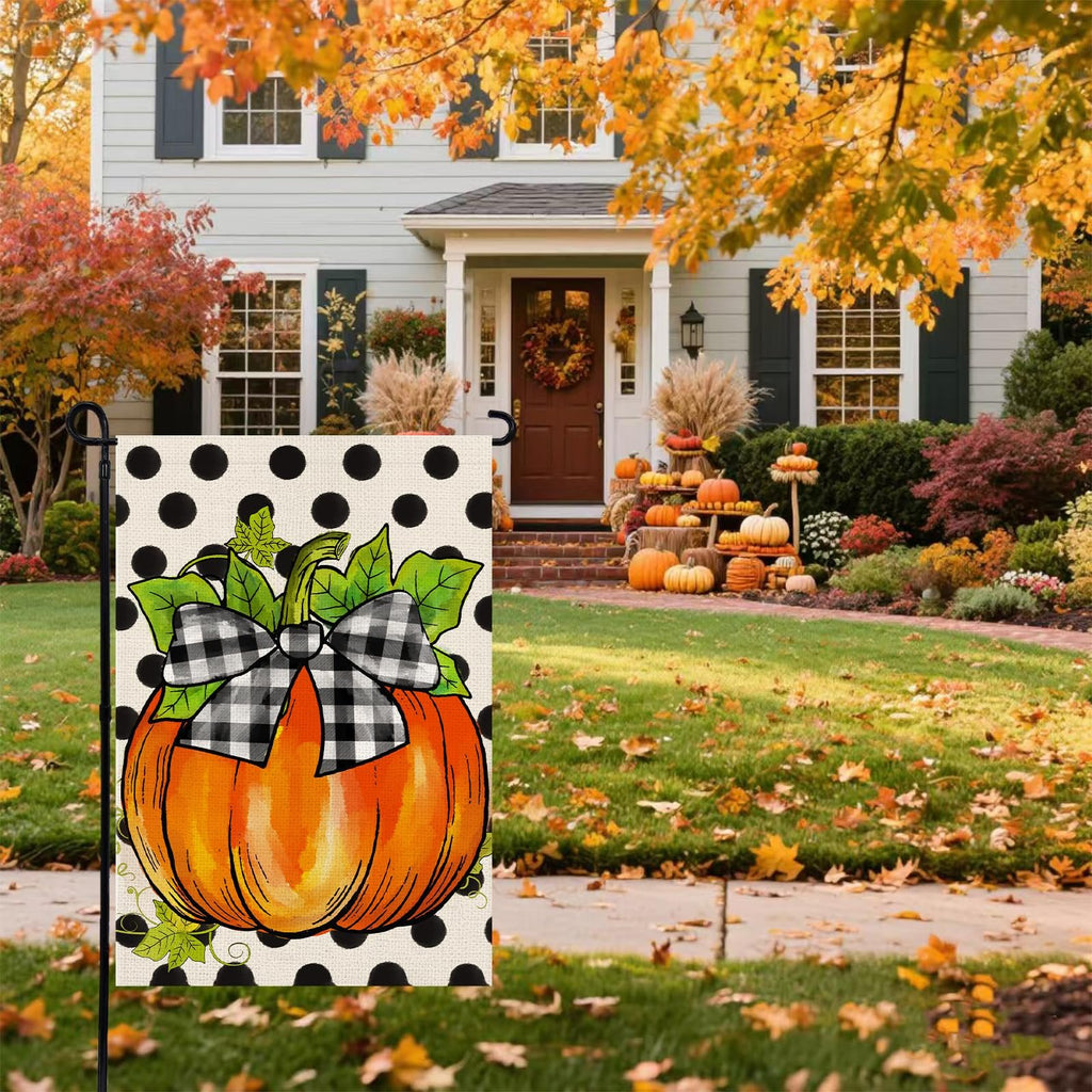 Garden flag with a pumpkin wearing a black and white buffalo plaid bow, set against a black polka dot background, displayed in front of a house decorated for fall.
