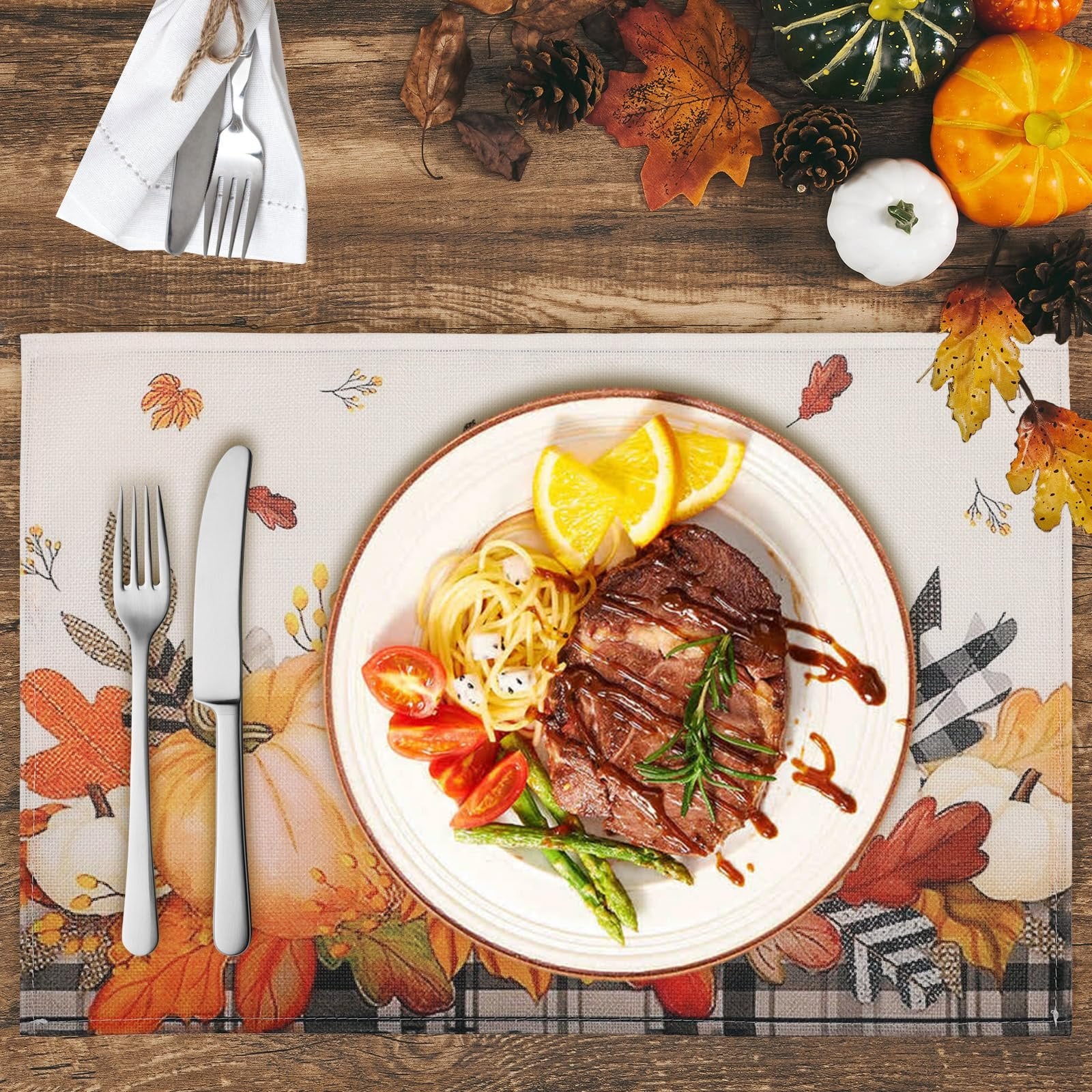 Autumn placemat with pumpkins and maple leaves, set with a plate of steak and pasta, and cutlery.