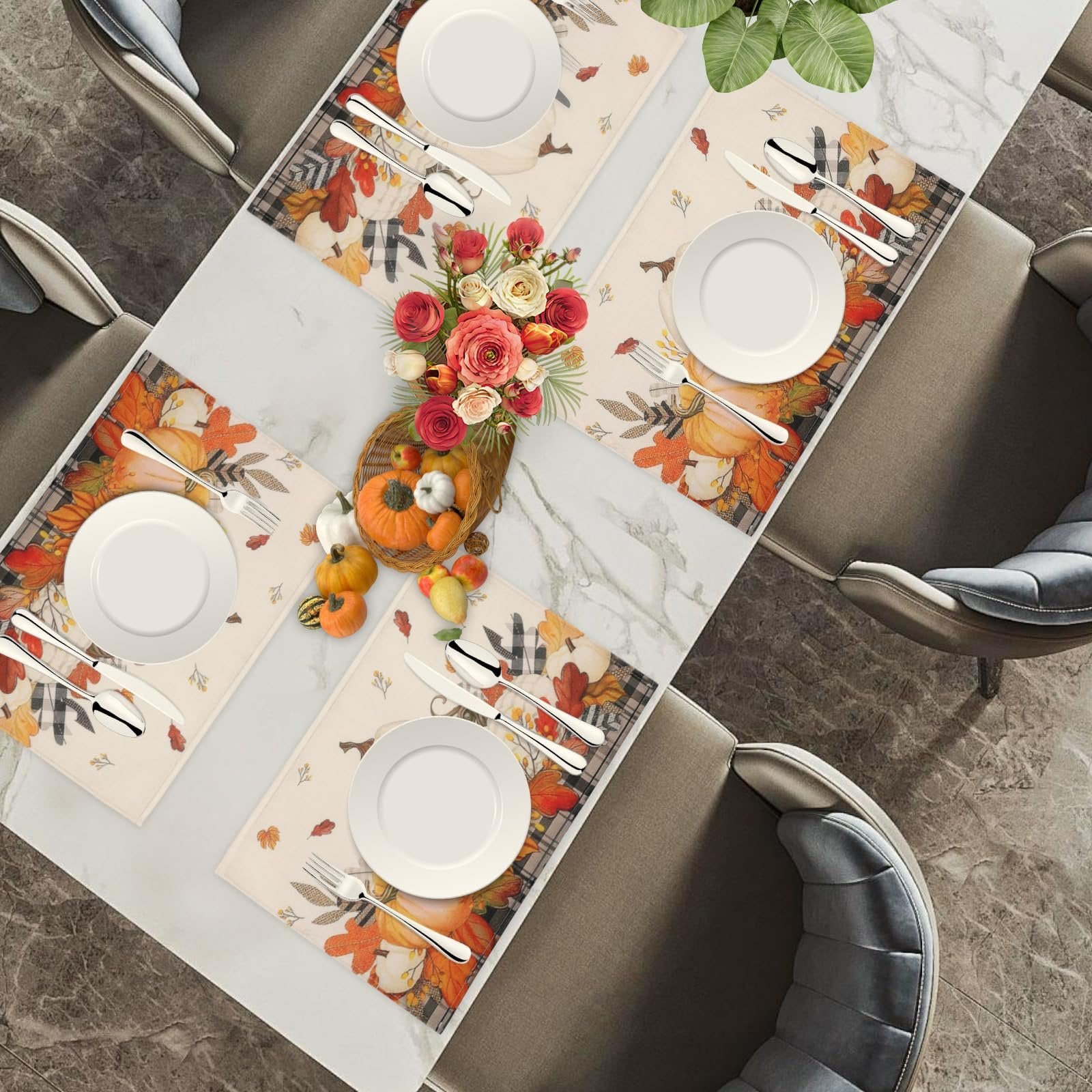 Set of four autumn placemats with pumpkin and maple leaf design on a dining table with place settings.