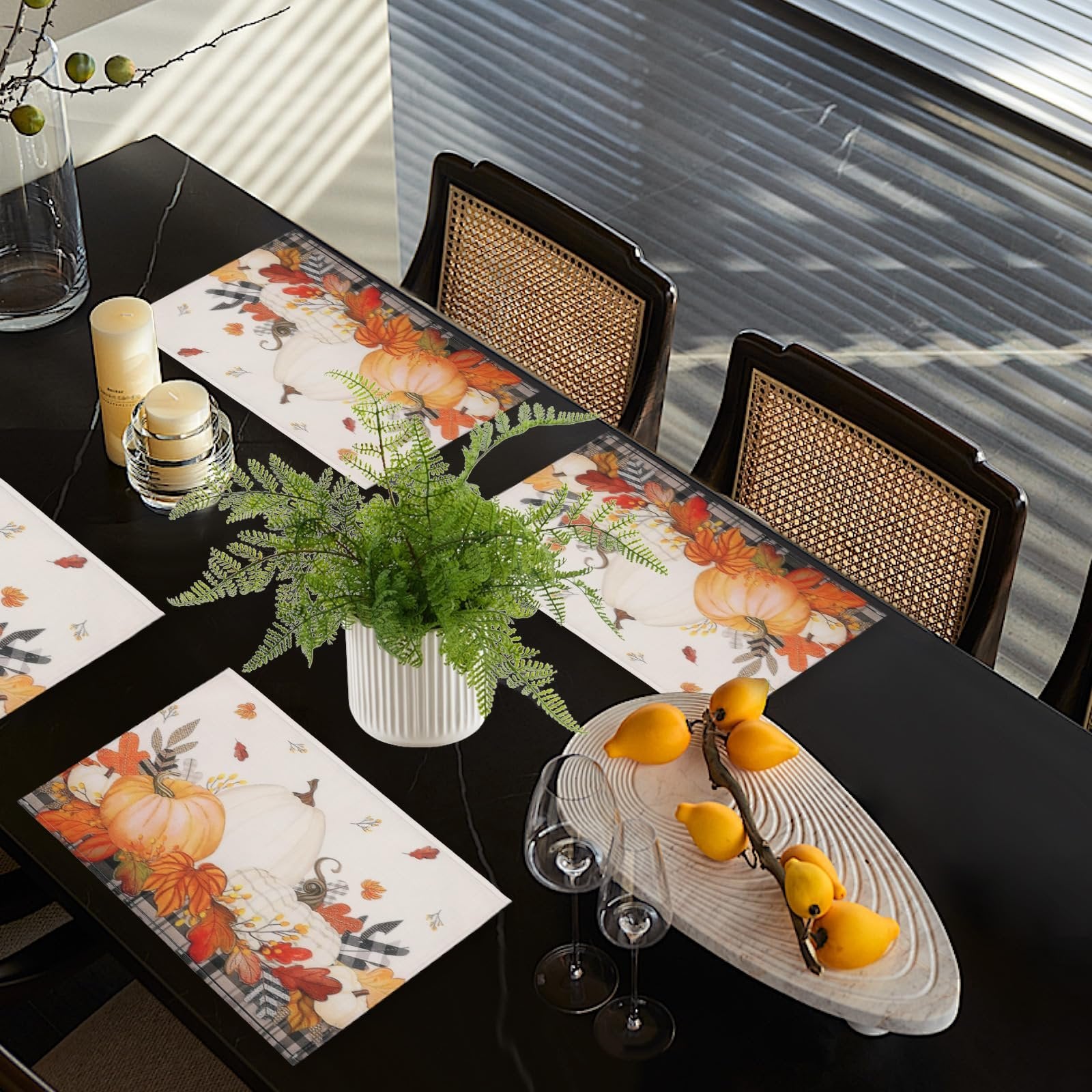 Set of four autumn placemats with pumpkins and maple leaves arranged on a black dining table with chairs and decorative items.