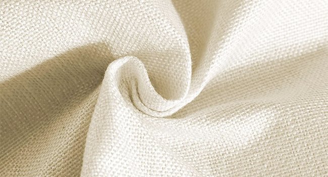 Close-up of textured beige fabric with soft folds and shadows, showing woven detail.