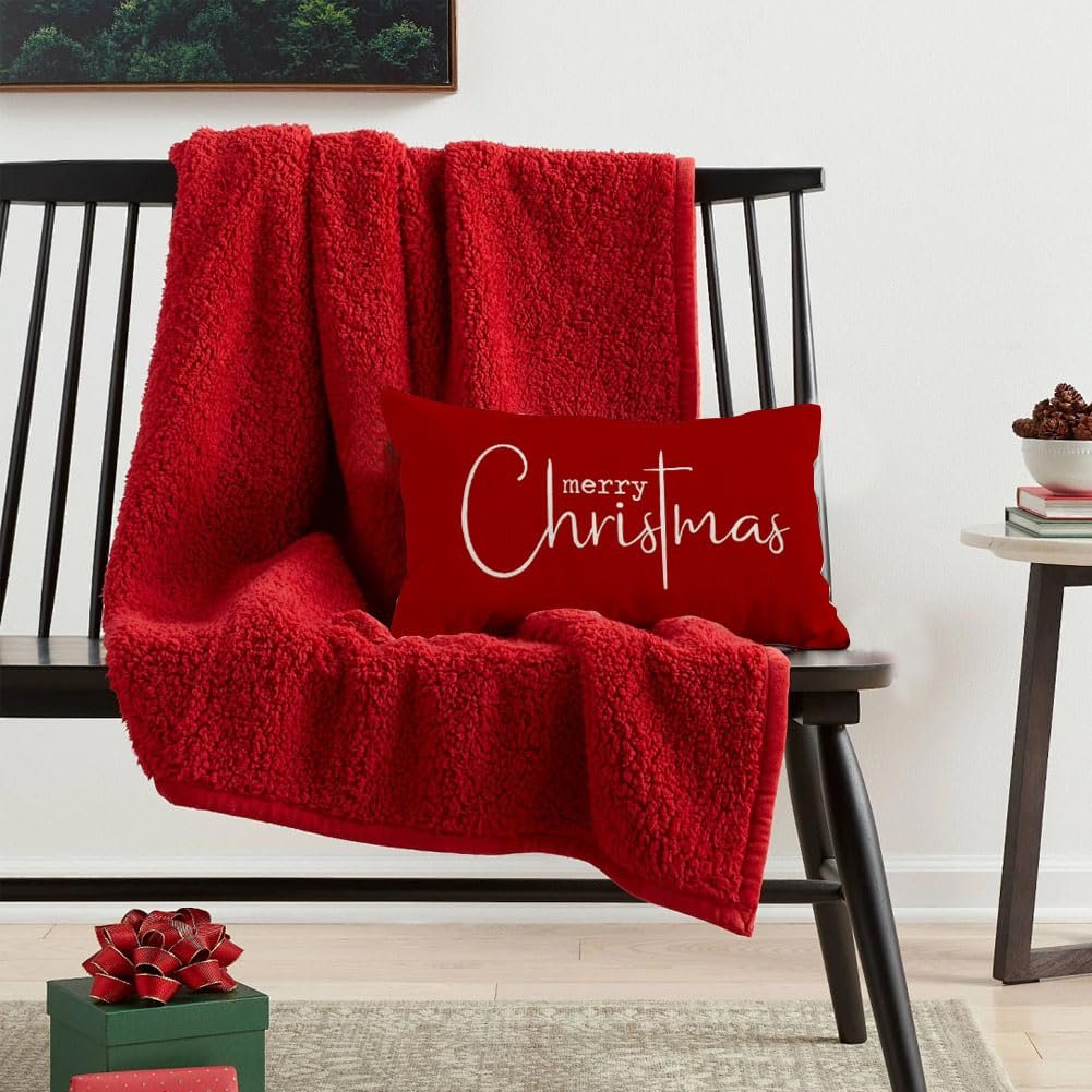 Red sherpa throw blanket draped over a black bench with a red lumbar pillow that says "merry Christmas" in white script.