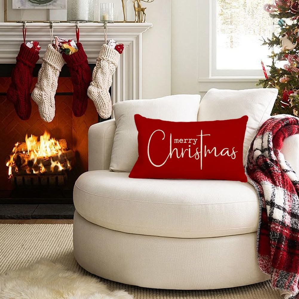 Red lumbar pillow with white 'merry Christmas' text on a white armchair by a fireplace.