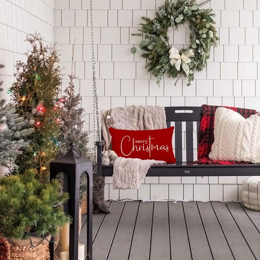 Red lumbar pillow with 'merry Christmas' text on a porch swing with Christmas trees and a wreath