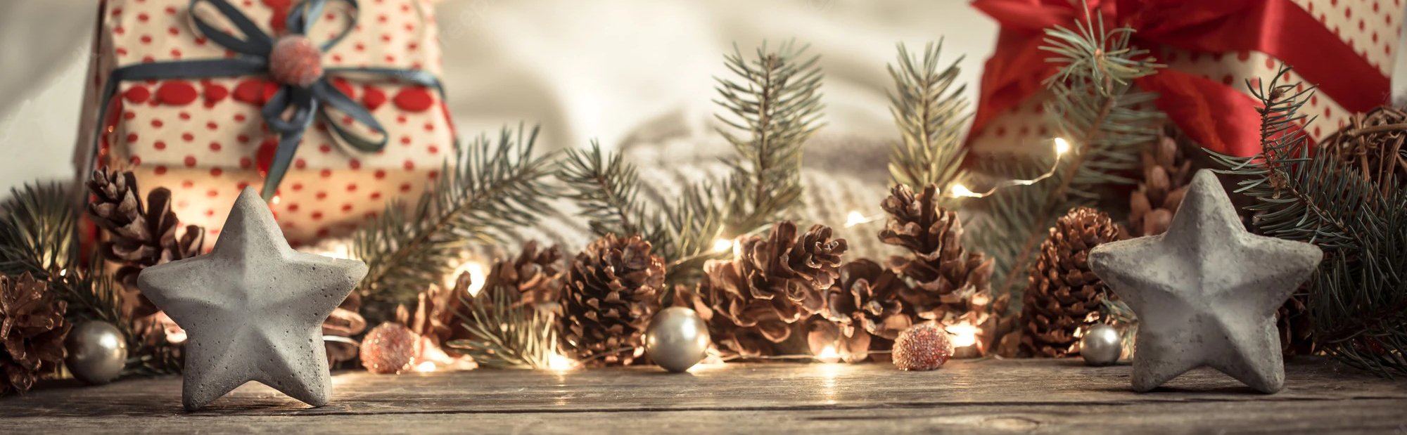 Christmas holiday decor with pinecones, fir branches, fairy lights, and star ornaments on a wooden surface.