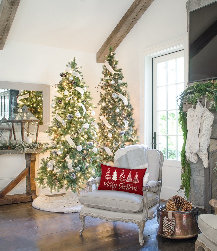 Christmas pillow with trees and 'Merry Christmas' text on a chair in a festive living room with trees and fireplace