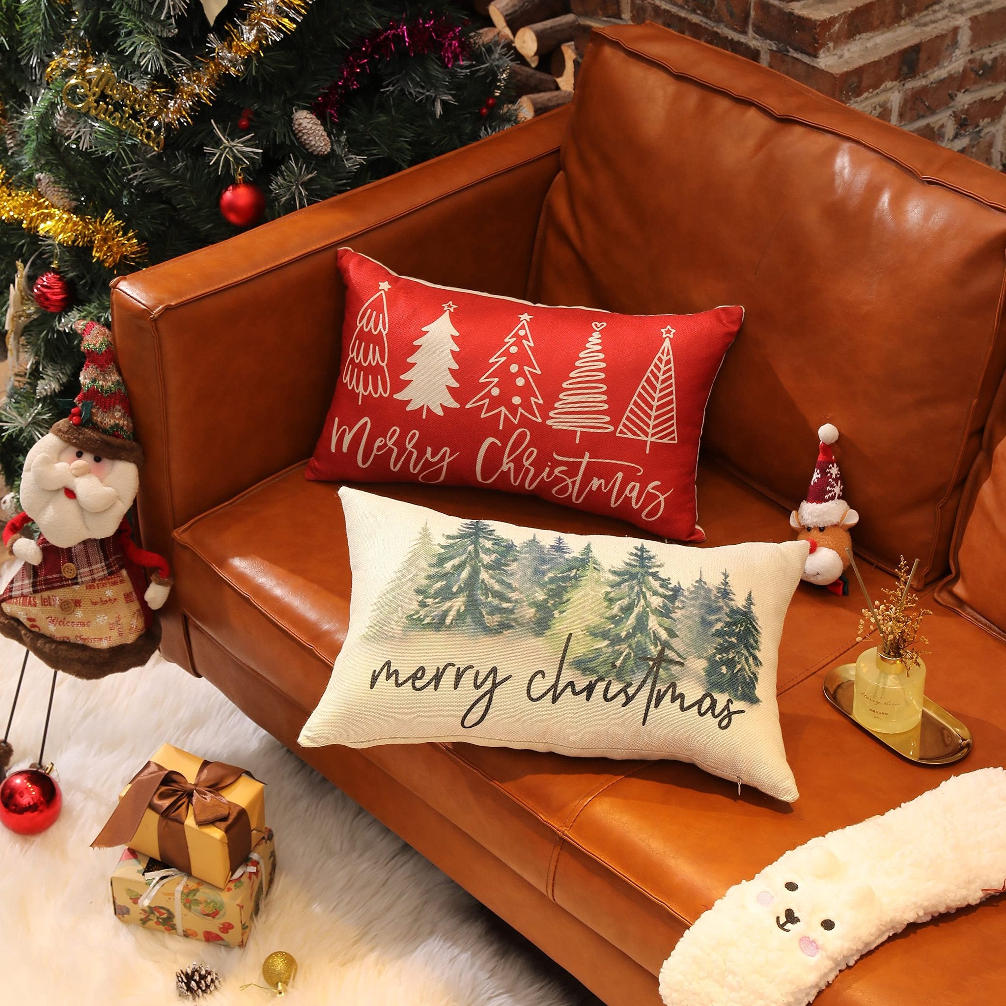 Two Christmas-themed lumbar pillow covers displayed on a brown leather couch next to a decorated Christmas tree.