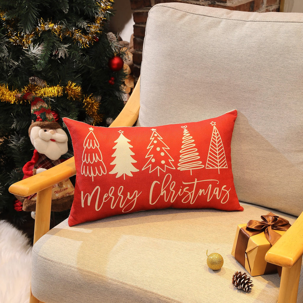 Red Christmas pillow cover with white trees and 'Merry Christmas' text on a chair next to a decorated tree.