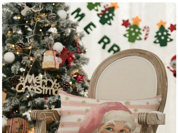 Close-up of a pink Santa Claus pillow cover with stripes and snowflakes, placed on a chair next to a decorated Christmas tree.