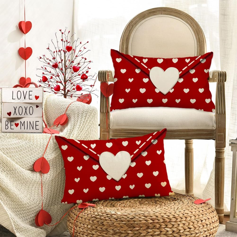 Two red lumbar pillow covers with white hearts and a large white heart on a chair and ottoman.