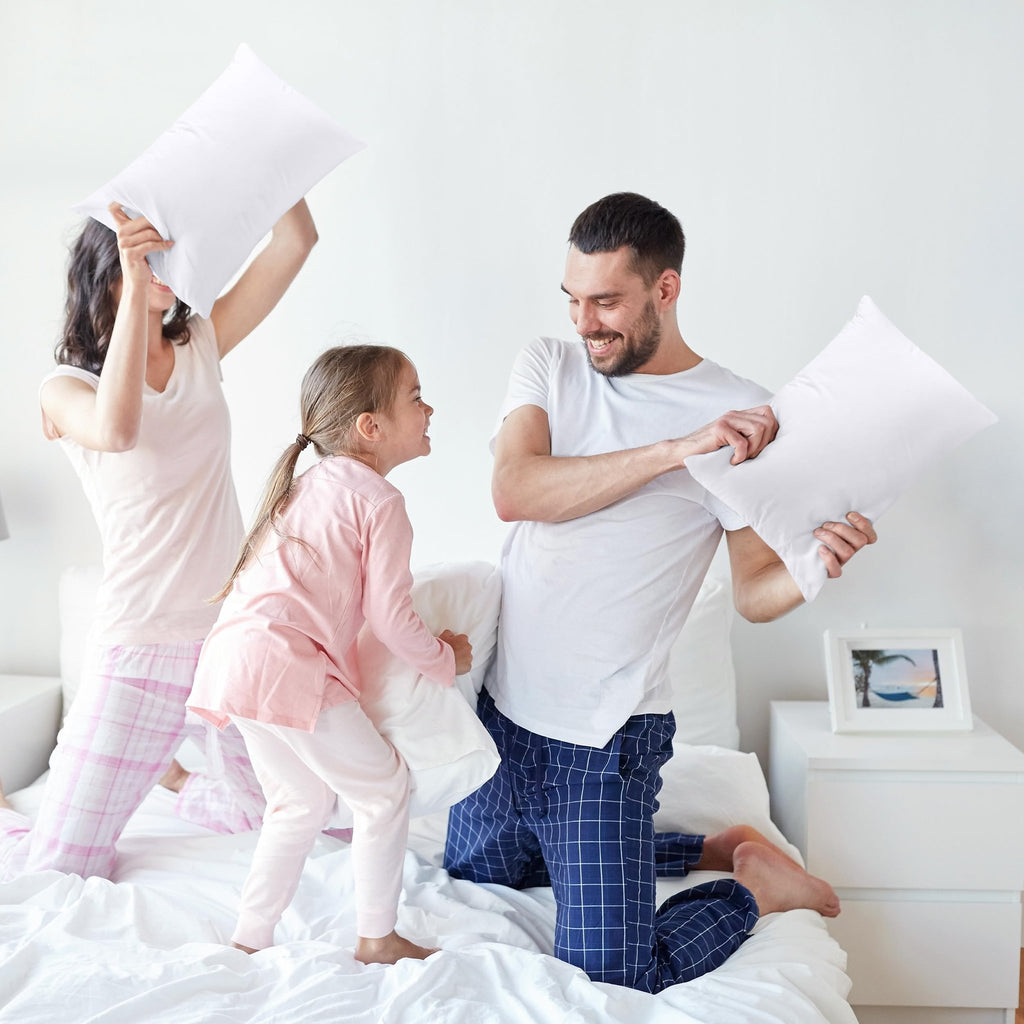 Family having a pillow fight on a bed with white pillows. A father, mother, and daughter are playing.