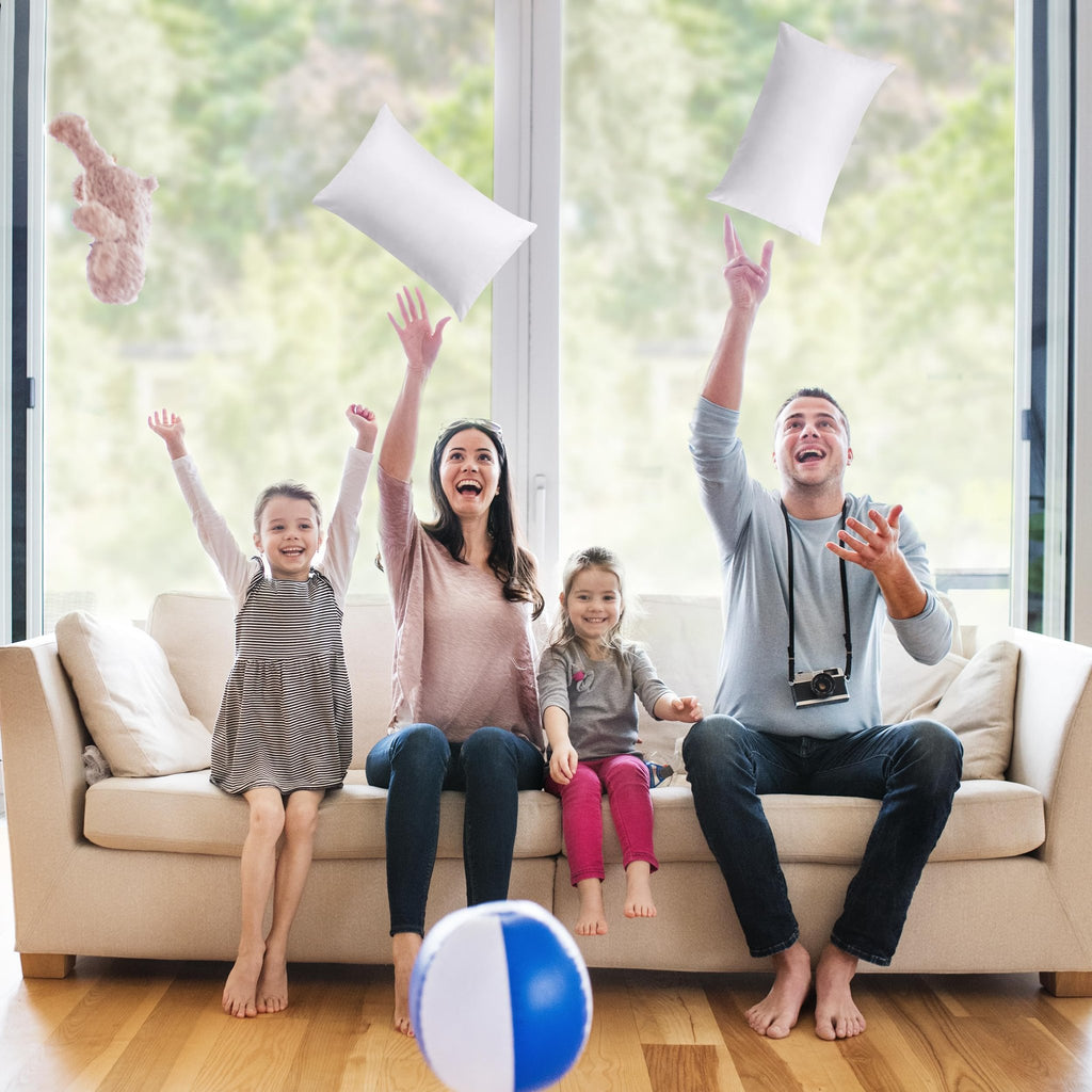 Family of four playing with white pillow inserts and a stuffed animal in a living room with a large window