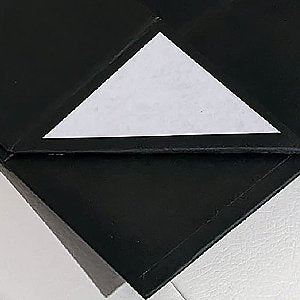 Close-up of a black magnetic gift box with a white paper triangle sticker on the lid.