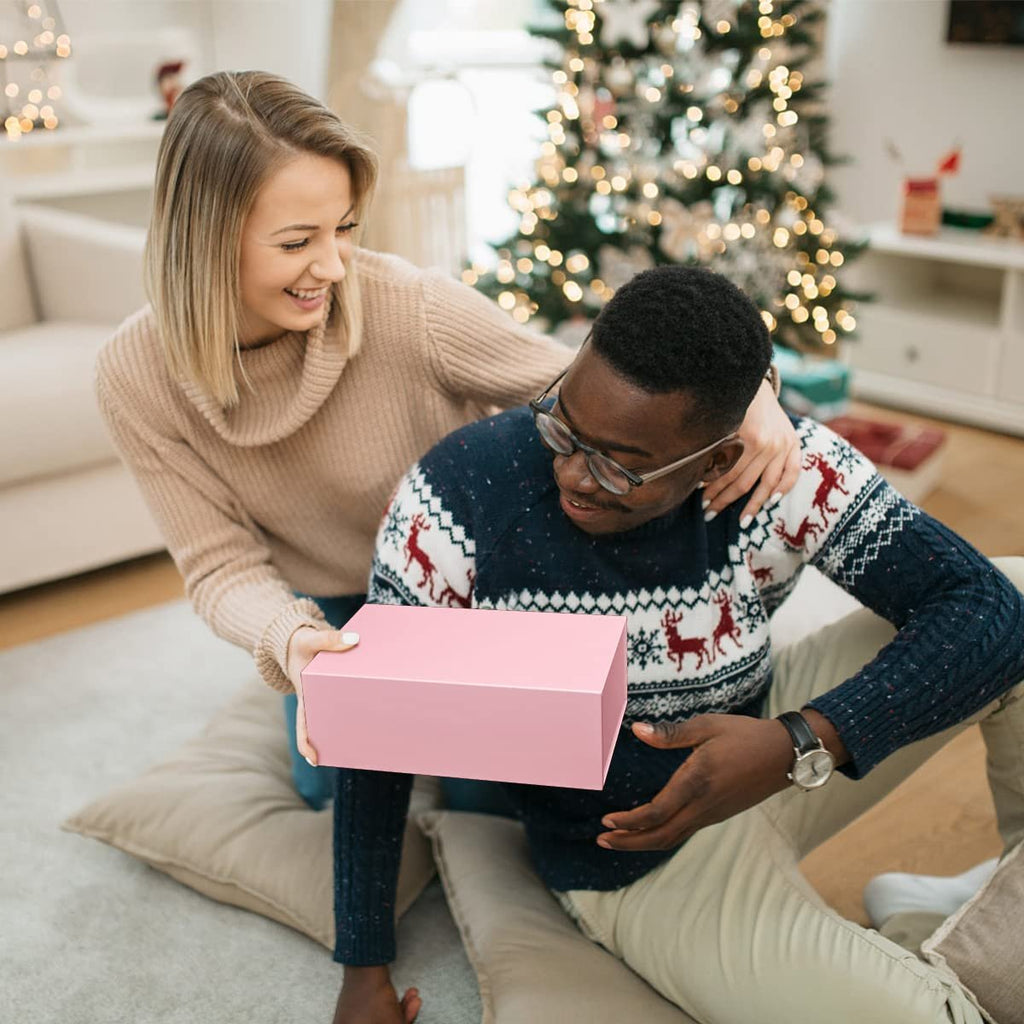 Woman giving a pink magnetic gift box to a man in front of a Christmas tree