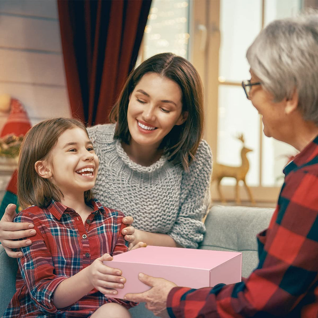 Woman giving a pink gift box to a smiling girl, with another woman looking on happily.