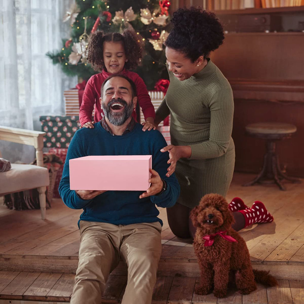 Family opening a pink gift box near a Christmas tree, with a dog present