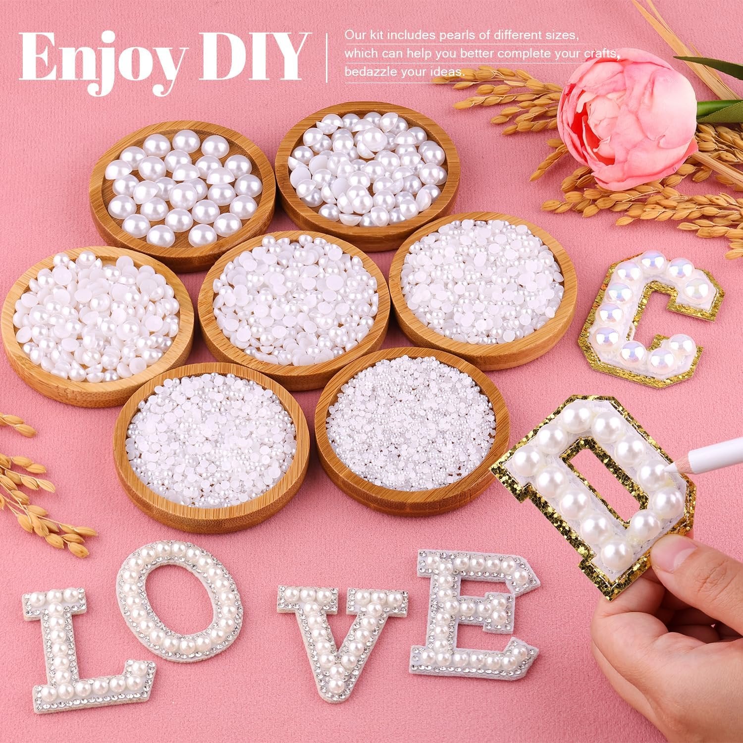 Flat lay of various sizes of white flatback pearls in wooden bowls, with letters spelling LOVE and C decorated with pearls, and a hand holding a decorating pen.