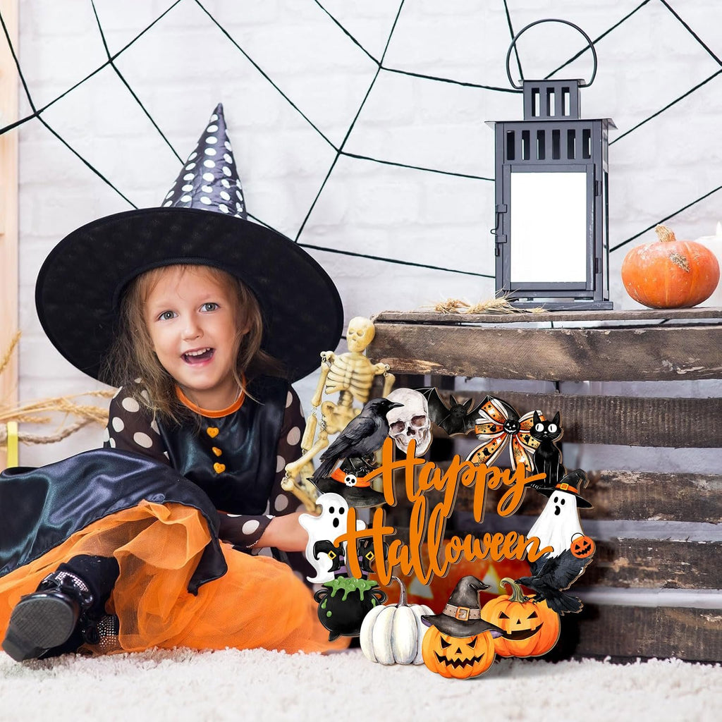 Young girl in witch costume sits next to a Happy Halloween door sign with pumpkins, ghosts, and a black cat.