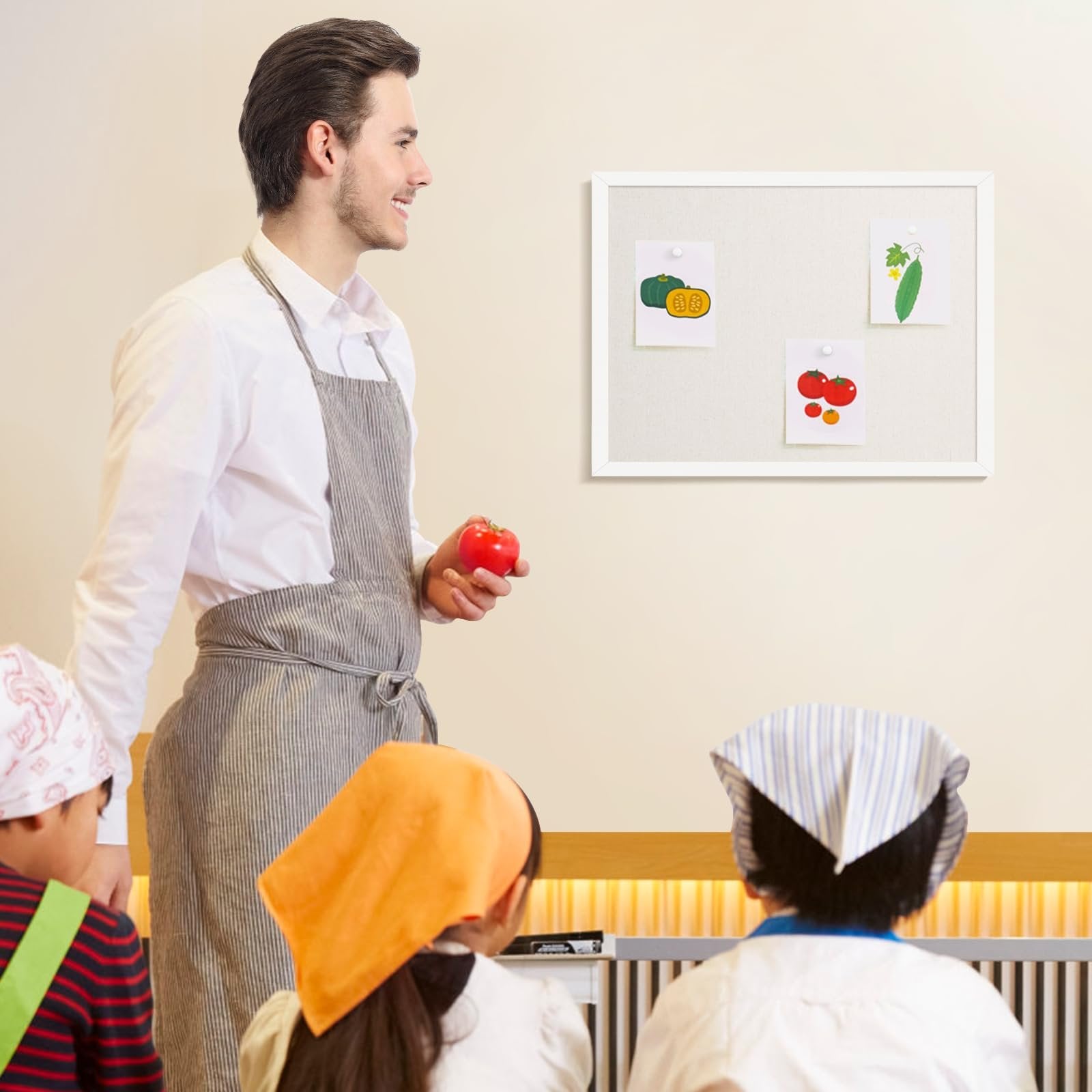 Man in apron holding tomato, facing bulletin board with drawings of vegetables