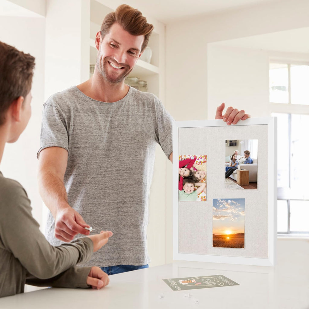 Man showing a linen bulletin board with white wood frame to a child, with photos pinned to it.