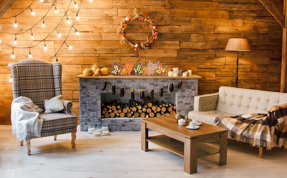 Cozy living room scene with a fireplace, plaid armchair, sofa, and coffee table decorated for fall with maple leaf lights.