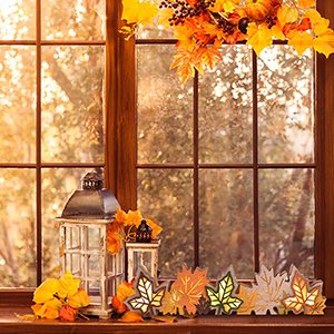 Wooden maple leaf blocks with LED lights arranged on a windowsill with a lantern and fall foliage decoration.