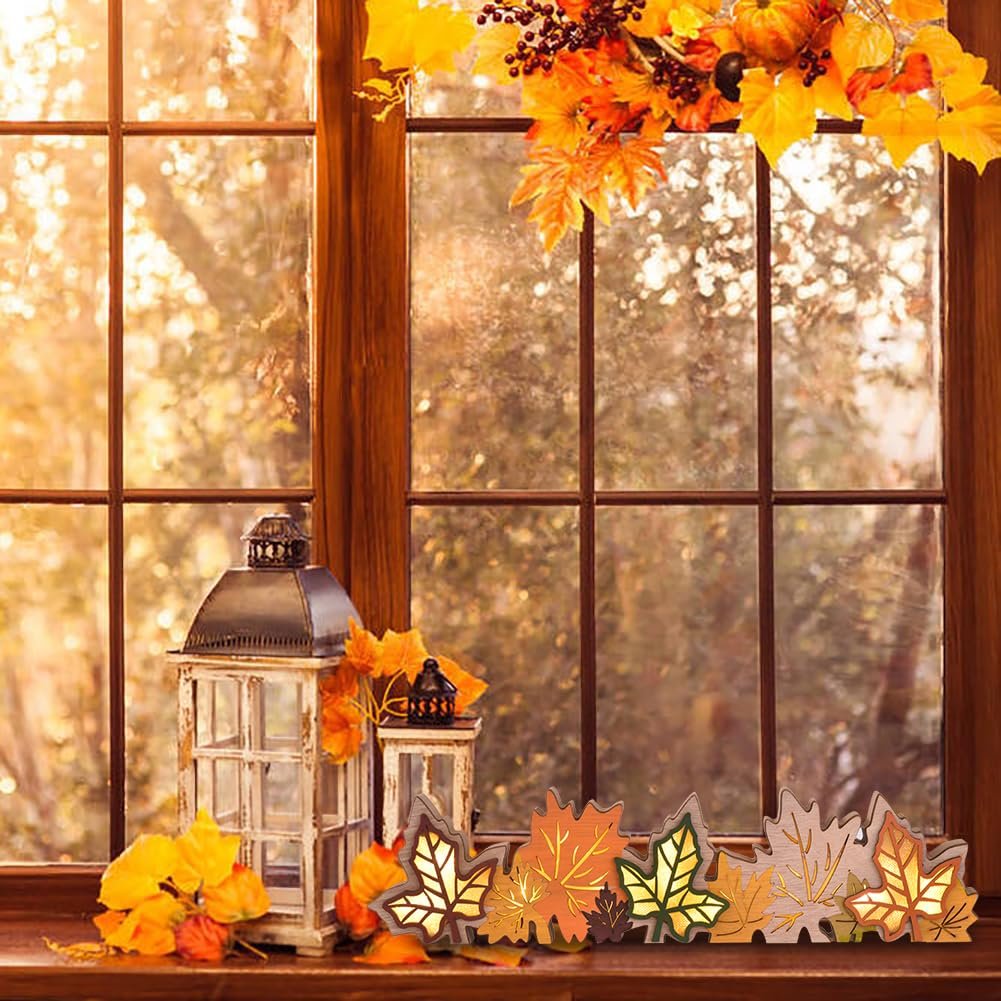 Wooden maple leaf block sign with LED lights on a windowsill with autumn decorations.