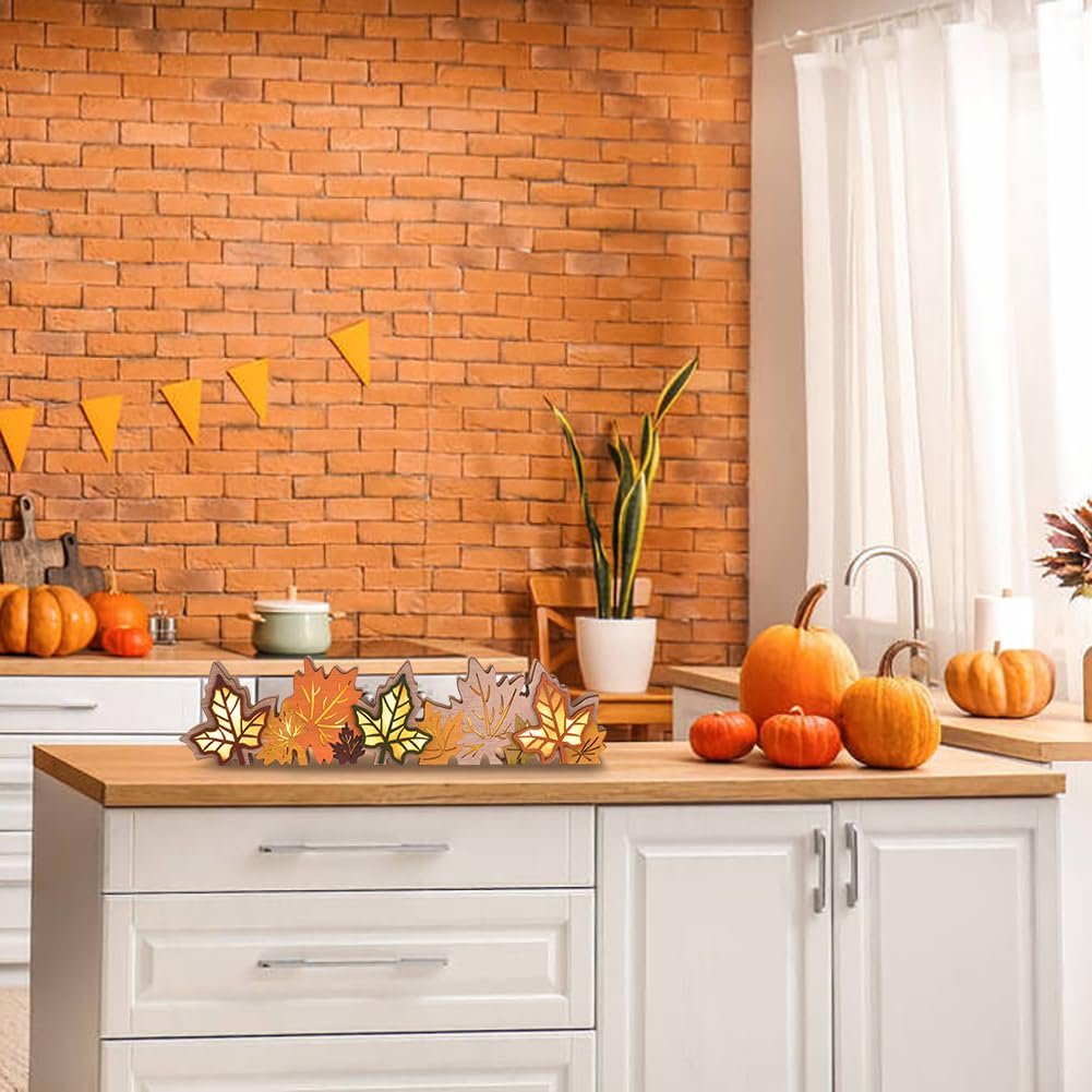 Wooden maple leaf centerpiece with LED lights on a kitchen counter with pumpkins and fall decorations.