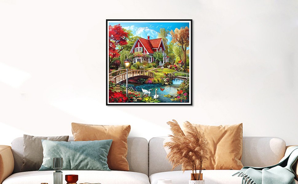 Countryside diamond painting kit featuring a red house, bridge, swans, and flowers, framed and hanging on a wall above a sofa.