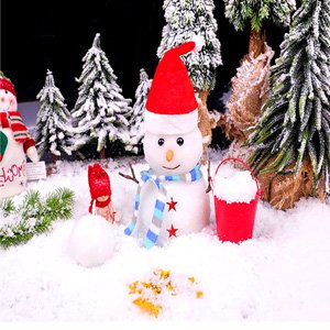 Christmas scene with a snowman, miniature trees, and artificial snow. A small red bucket is filled with snow.
