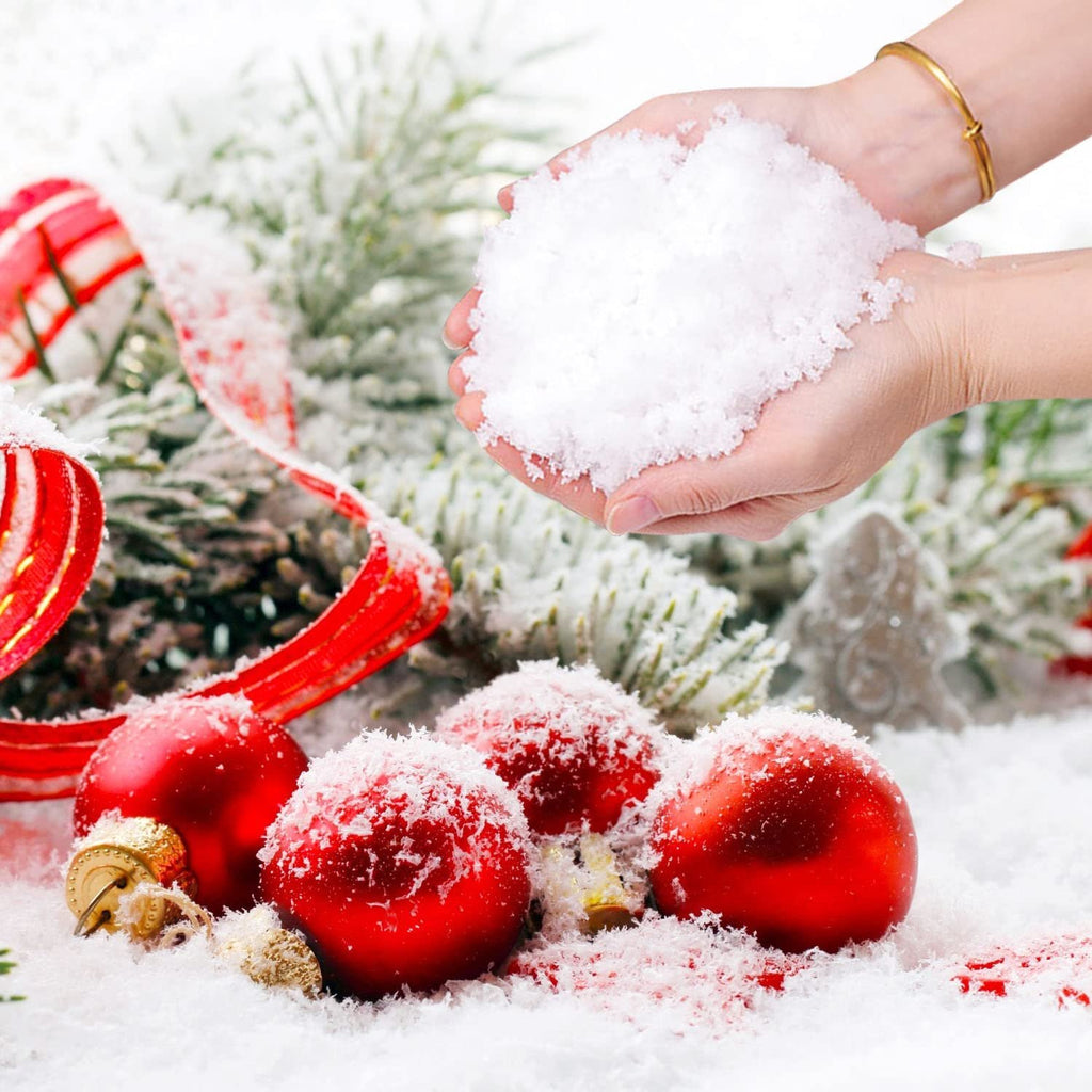 Hands holding artificial snow with Christmas ornaments and ribbon on a snowy background