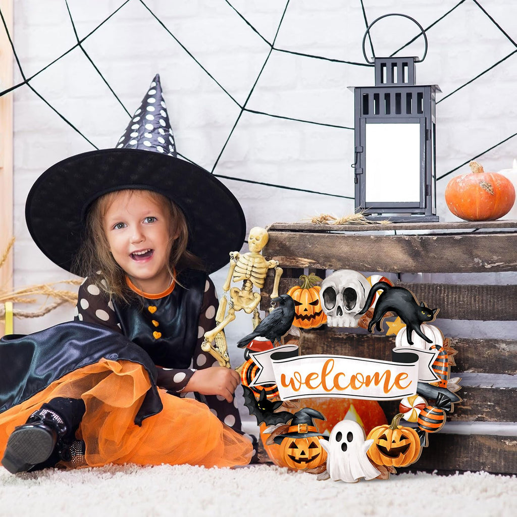 Girl in witch costume sitting next to Halloween wreath with welcome sign, skeleton, and lantern