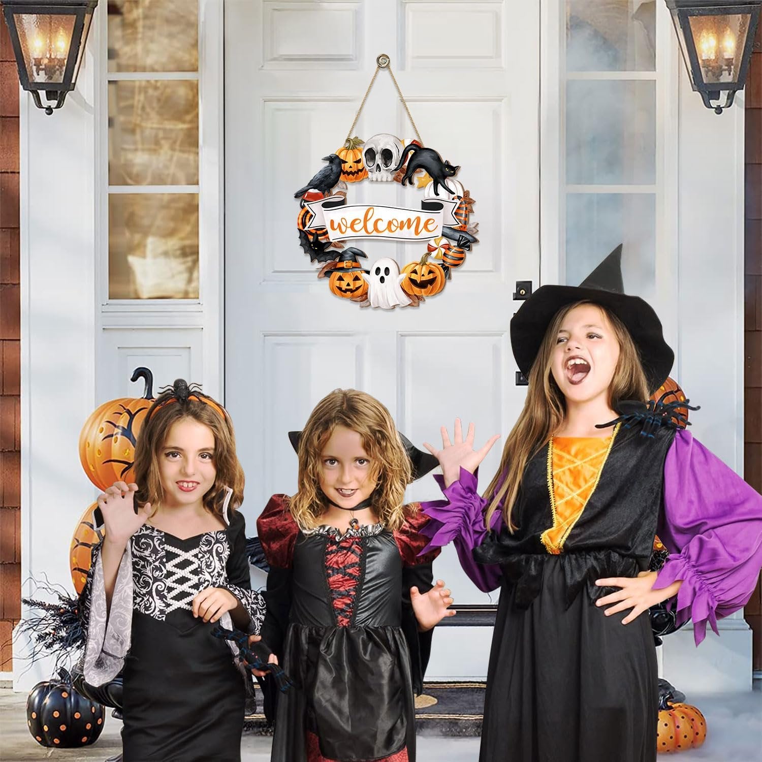 Three girls in Halloween costumes posing in front of a decorated door with a welcome wreath