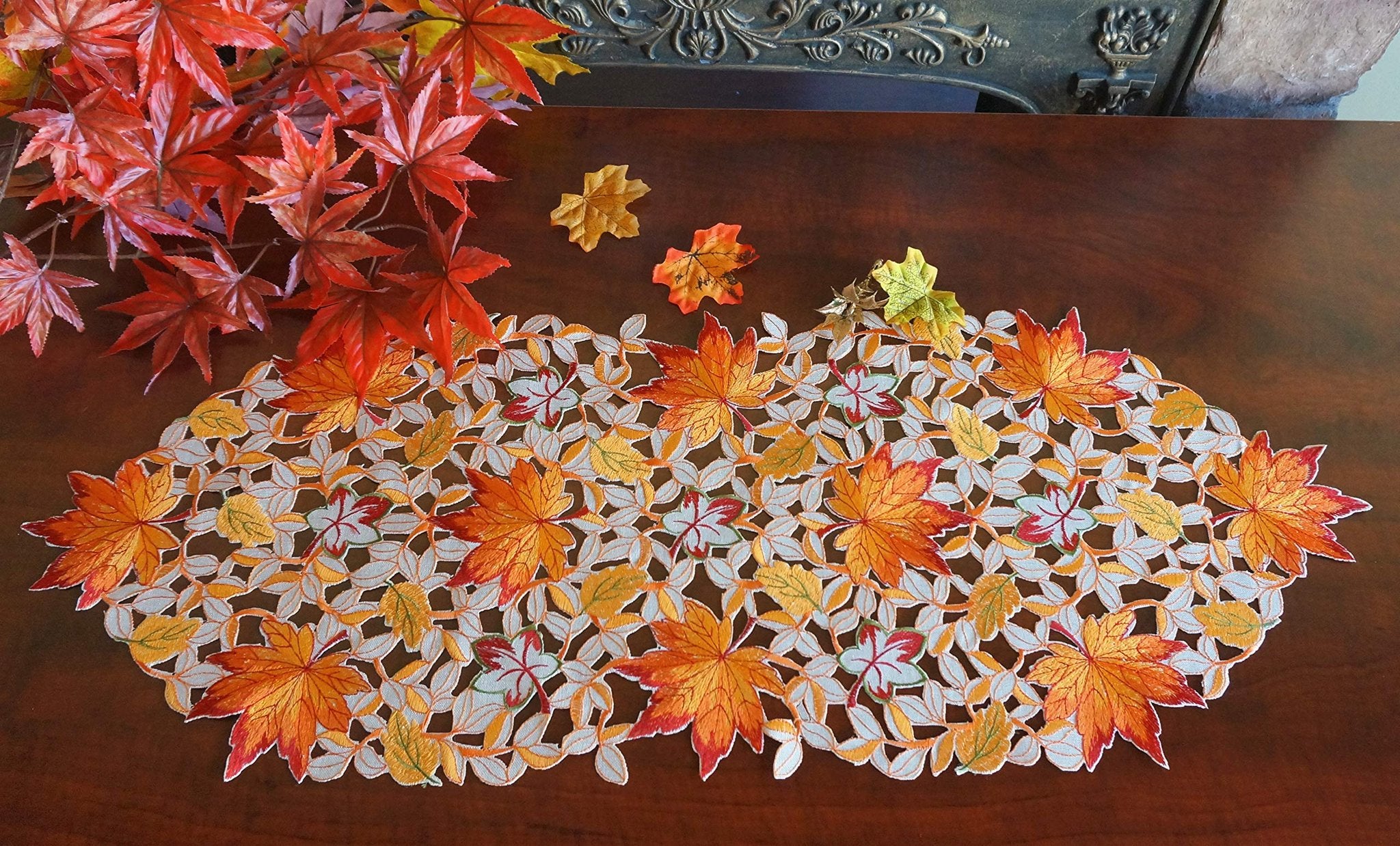 Fall table runner with embroidered pumpkins, maple leaves, and bats on a wooden table.