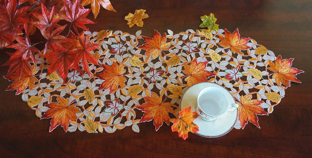 Fall table runner with embroidered maple leaves and bats, shown with a teacup and saucer on a wooden table.