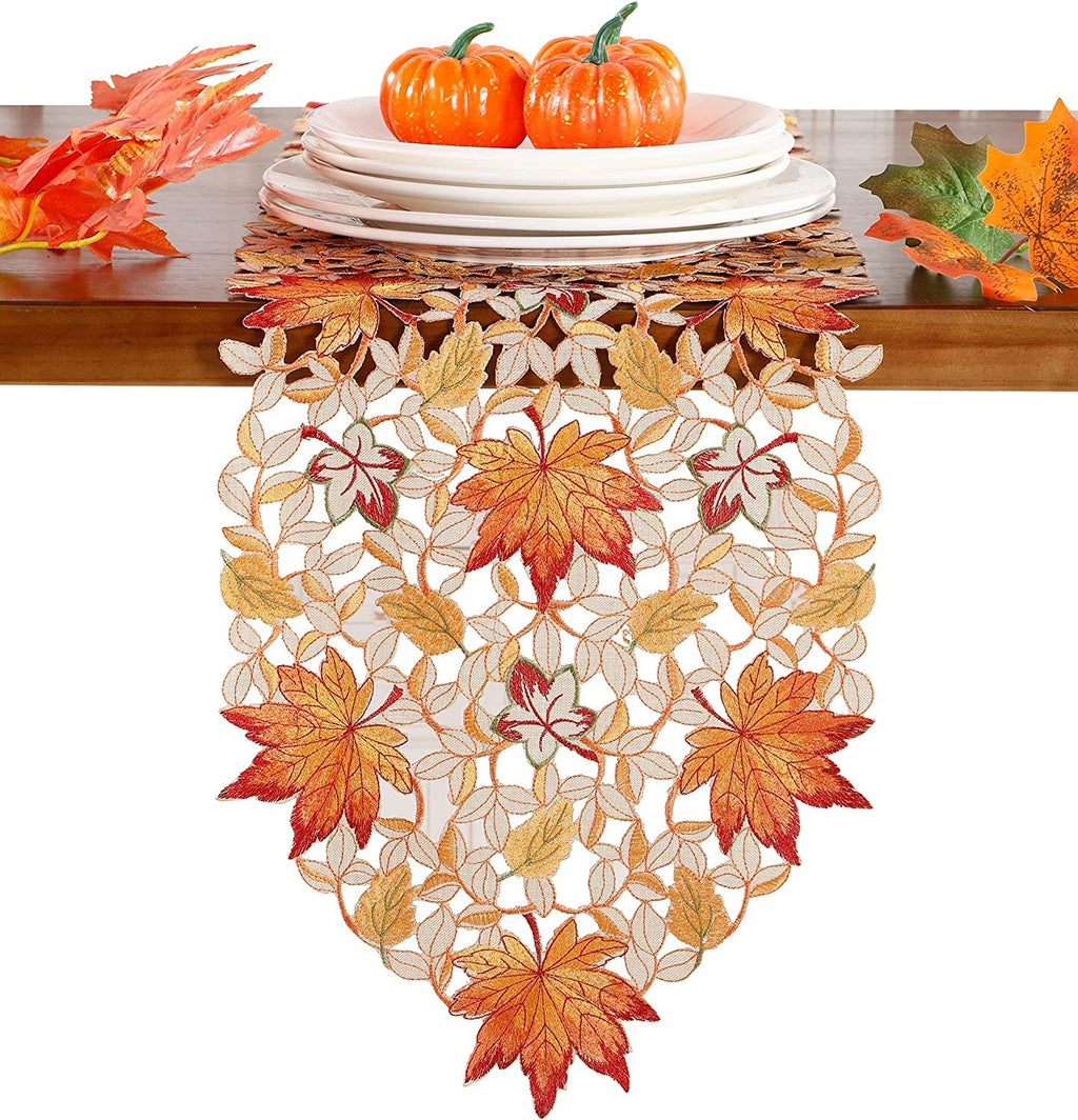 Fall table runner with embroidered pumpkins, maple leaves, and bats on a wooden table with plates and decorative leaves.